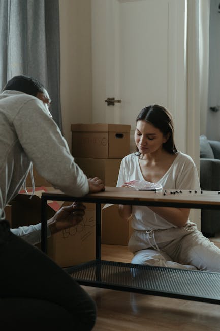 A young woman with long dark hair, dressed in a white t-shirt, is seated on the floor, carefully wrapping a small item with bubble wrap and securing it with tape, preparing fragile belongings for a ho